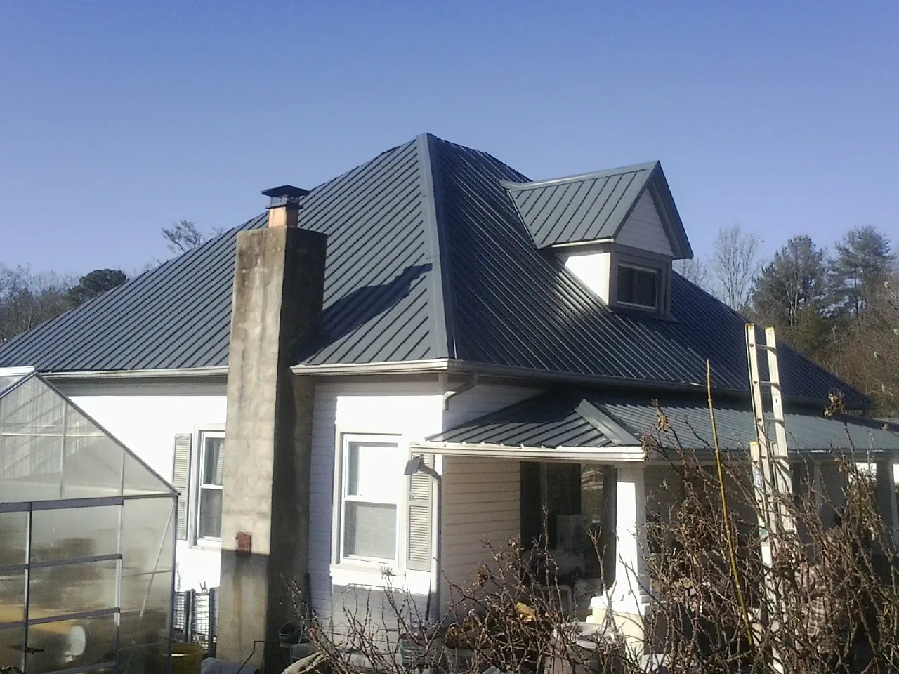 Dark blue standing seam metal roof on a white farmhouse with dormer — Slate & Tile Roof Repair by Roofing Brothers in Conklin