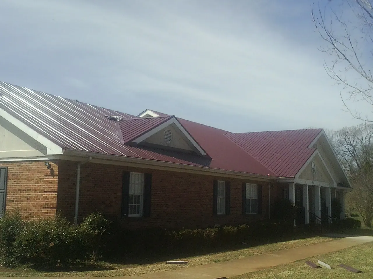 Red metal roof with gabled entries on a long brick building, from a Hail Damage Roof Repair job in Conklin