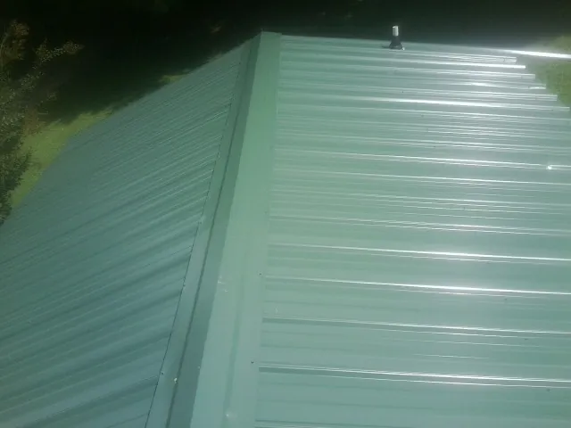 New green metal panels meeting at the ridge of a roof — Flat Roof Repair work by our crew in Conklin